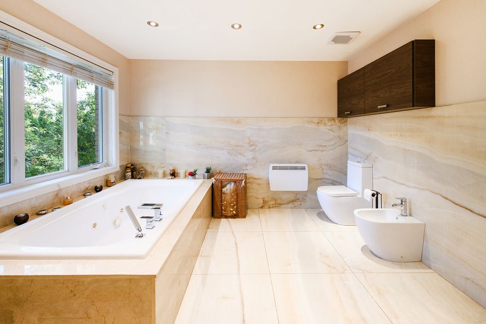 Luxurious master bathroom with marble tiles, soaking tub, bidet, and toilet in a bright beige elegant space.