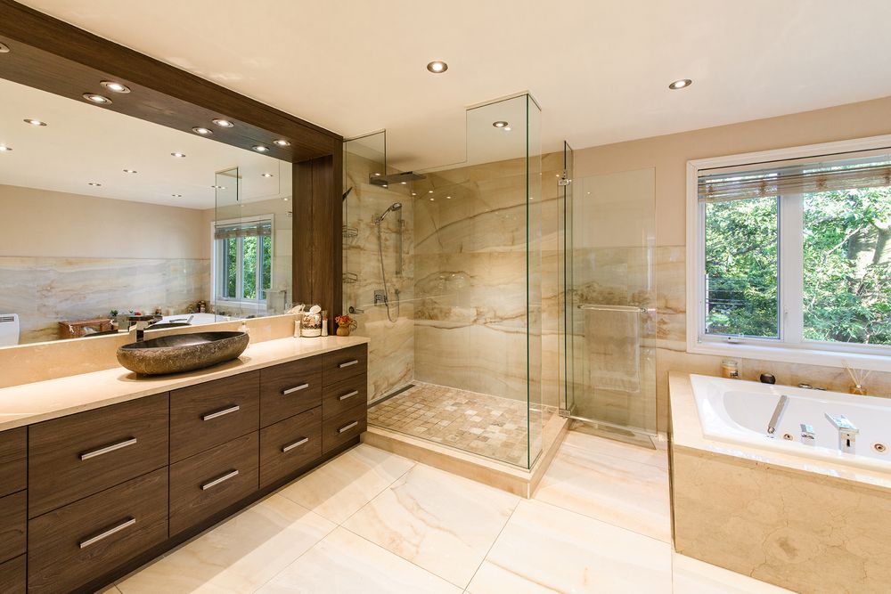 Modern bathroom featuring glass shower, dark wood vanity, large mirror, and marble tiles with natural light.
