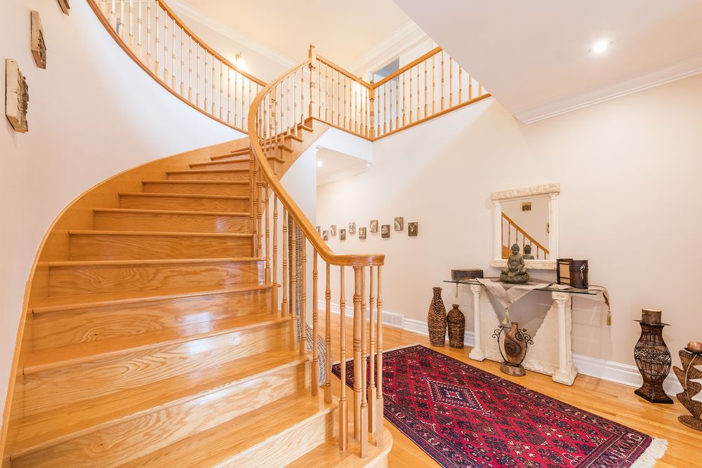 Elegant curved oak staircase with white balusters, hardwood floors, and a decorative red Persian rug.