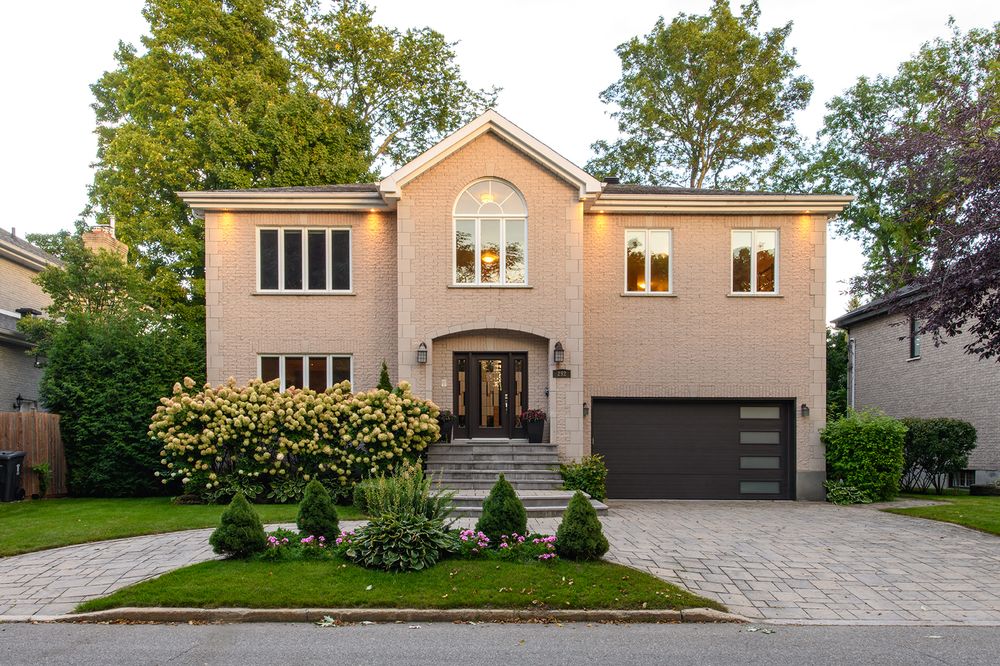 Stunning two-story brick home with arched windows, manicured landscaping, and a paved driveway at dusk.