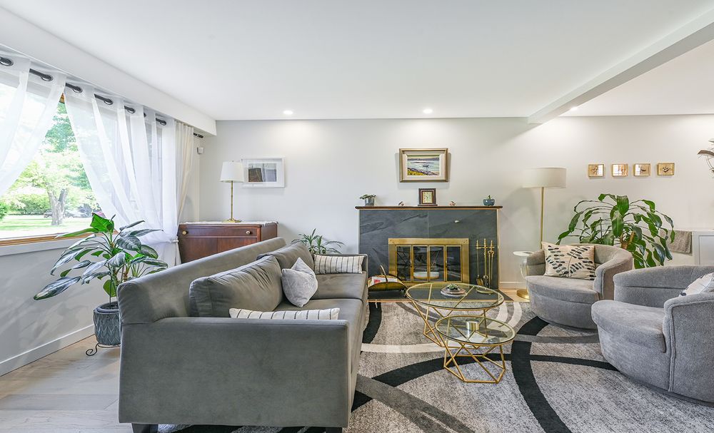 Elegant living room with gray sofas, gold coffee table, fireplace, and lush plants on hardwood floors.