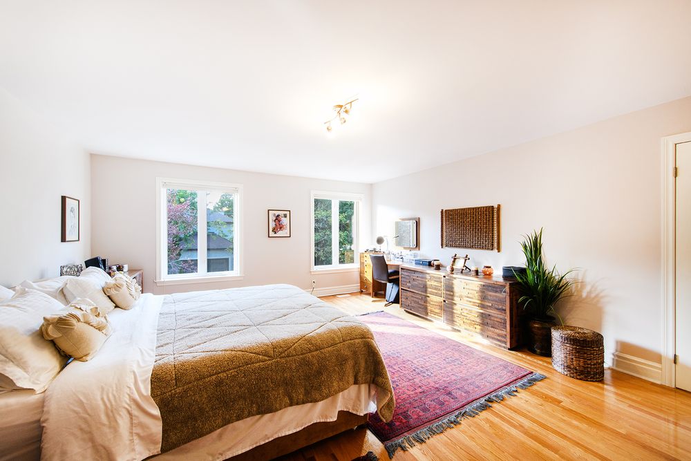 Bright spacious master bedroom with hardwood floors, large windows, and a colorful Persian area rug.