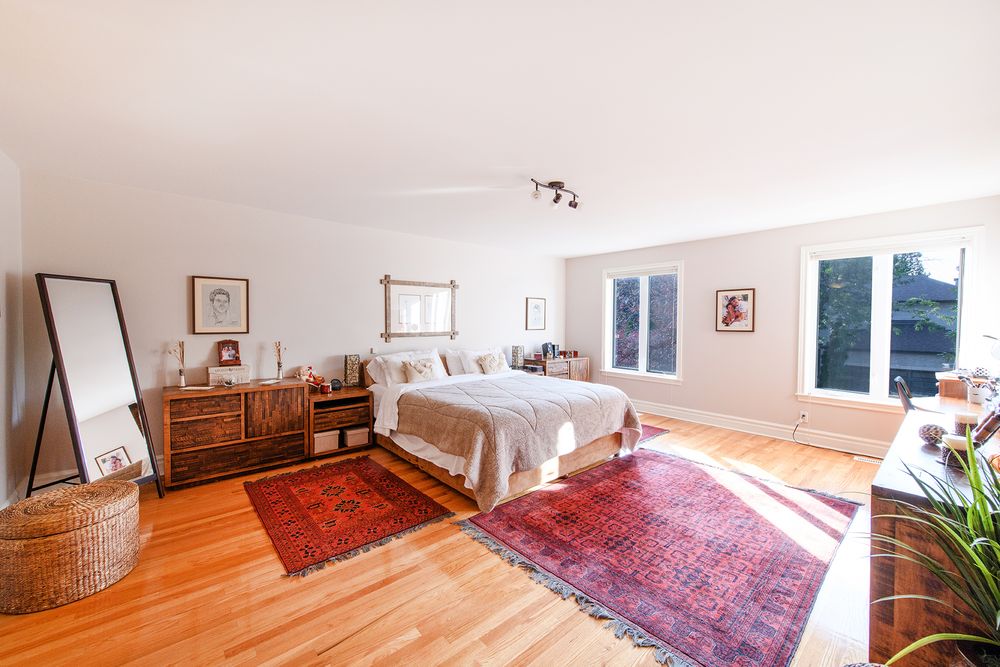 Airy master bedroom with hardwood floors, red Persian rugs, natural light, and a full-length mirror.