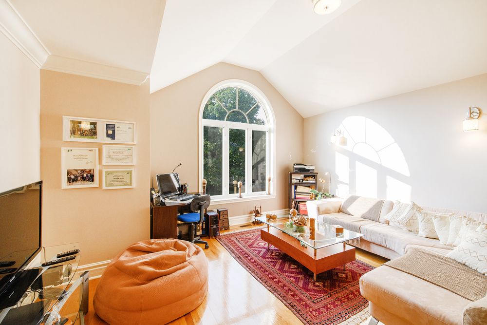Bright living room with vaulted ceiling, arched window, hardwood floors, red Persian rug, white sofa, and bean bag chair.