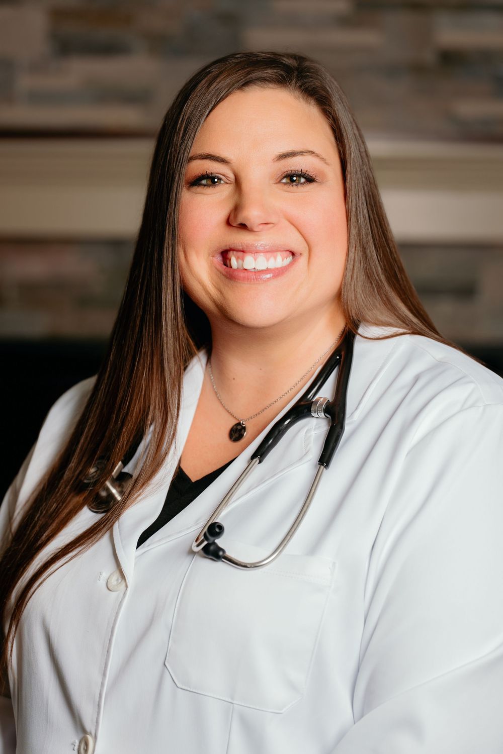 Female healthcare professional in white lab coat with stethoscope smiling confidently in a medical office setting.