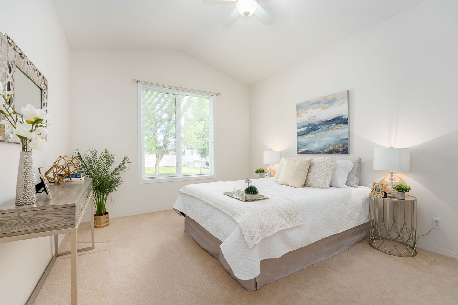 Bright white bedroom with vaulted ceiling, large window, neutral carpet, queen bed with white bedding, and coastal wall art.
