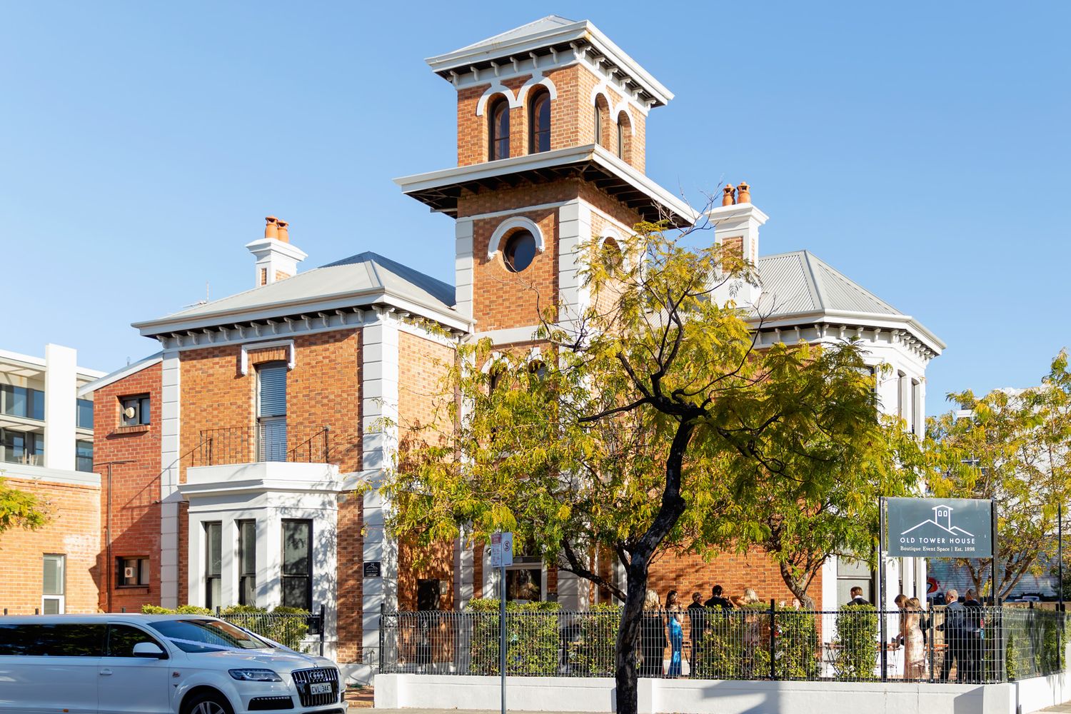 Historic brick building with clock tower surrounded by autumn trees under a clear blue sky in an urban setting.
