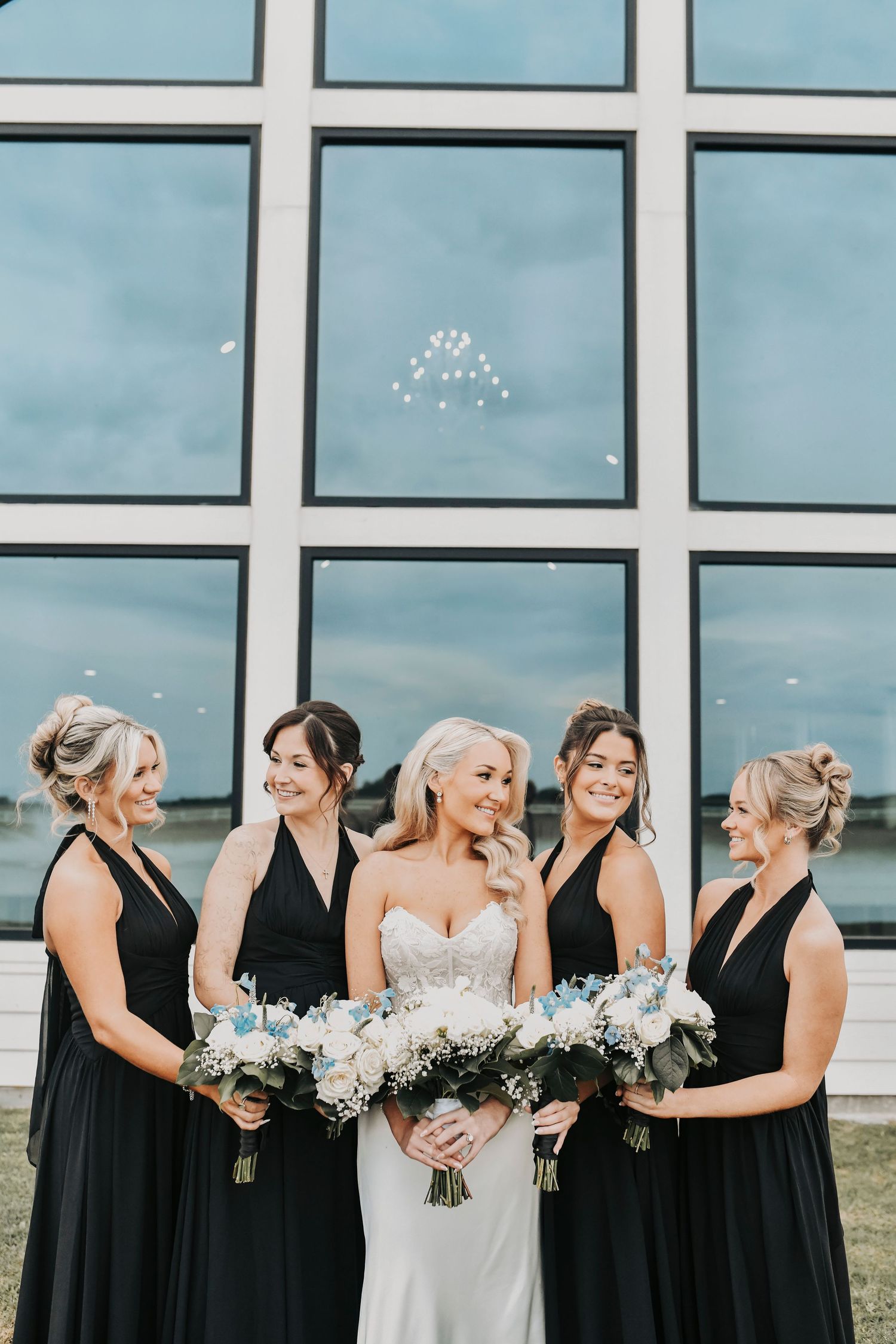 Bridesmaids in elegant black gowns holding white and blue bouquets