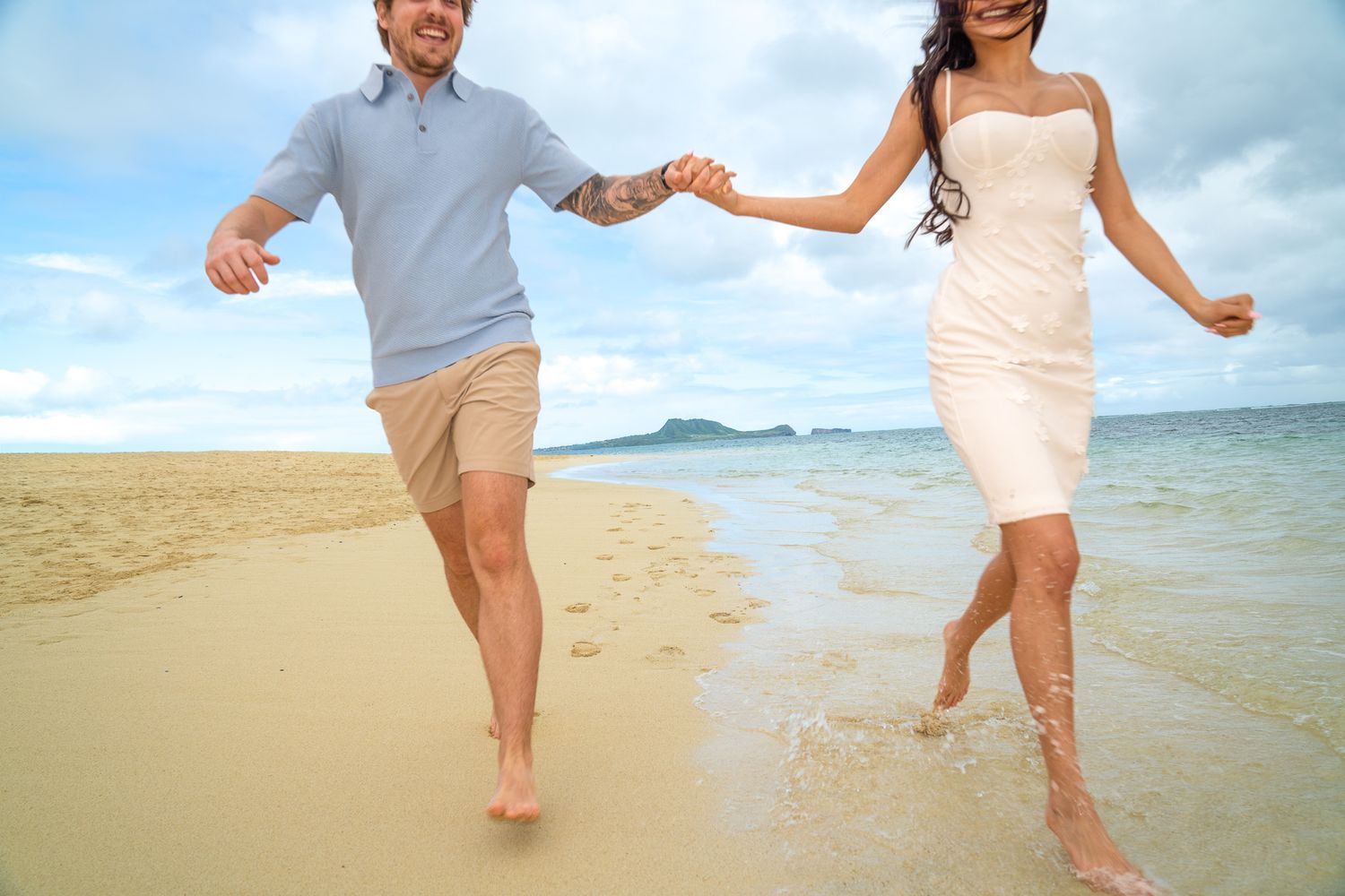 Happy couple holding hands running barefoot on a tropical beach with turquoise water and sandy shore.