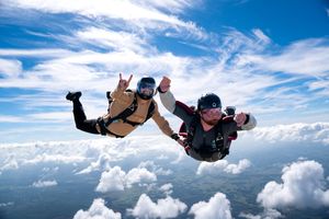 Two skydivers holding hands mid-air above clouds during a thrilling freefall skydiving adventure on a sunny day.