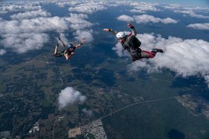 Two skydivers free falling above clouds and green landscape below.