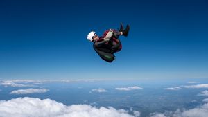 Skydiver freefalling above clouds against a vivid blue sky in a tucked position during a solo skydive.