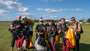 Group of skydivers posing with colorful parachutes on a green airfield after a successful jump.