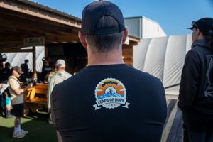 Man wearing a black Leaps of Hope t-shirt at an outdoor event with wooden benches.
