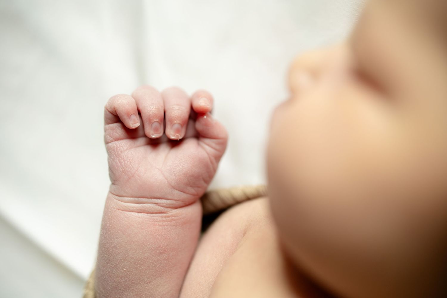 Close-up of a newborn baby's tiny clenched fist resting on a white blanket.