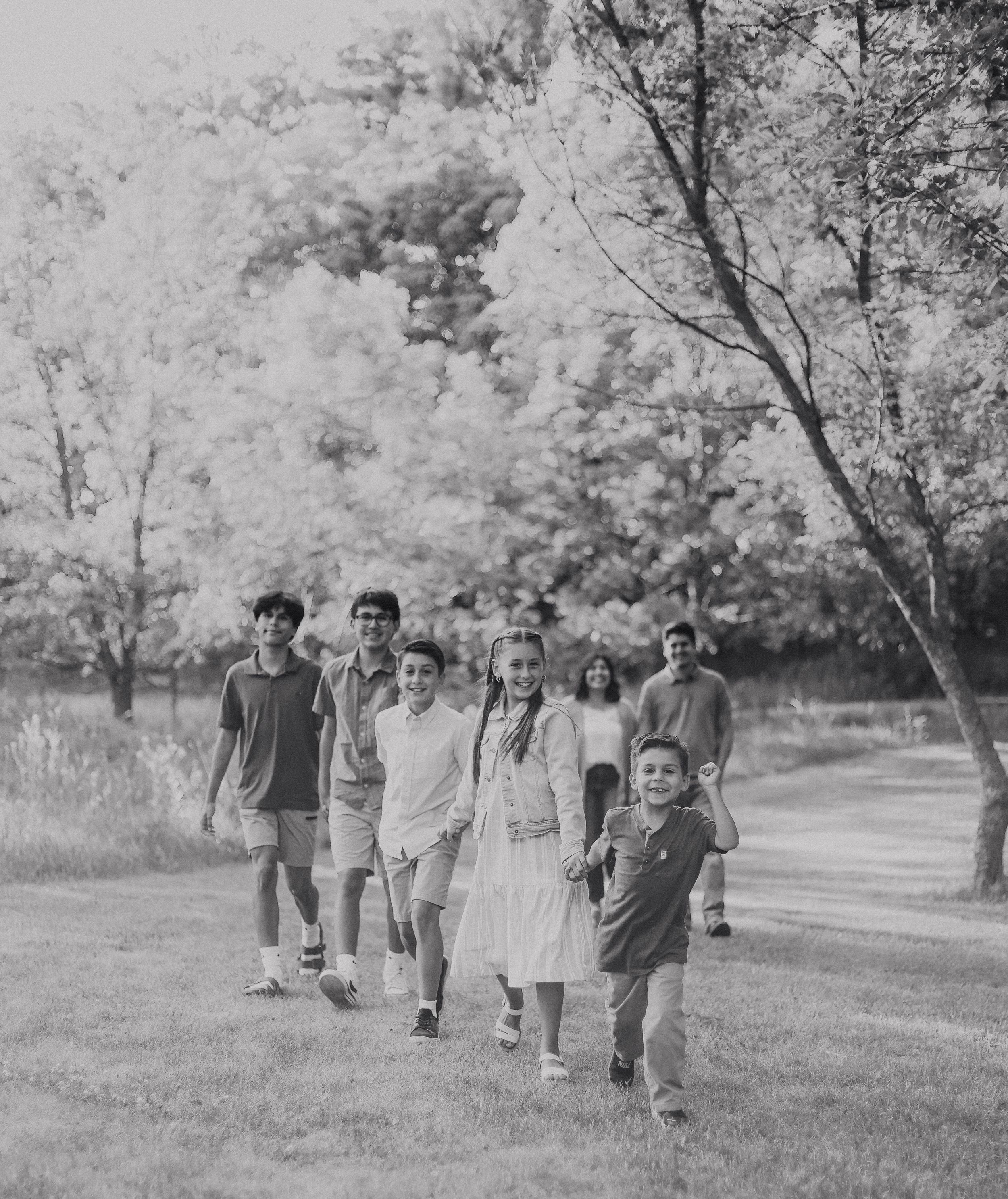 Black and white photo of a group of children and adults walking together through a lush green park on a sunny day.