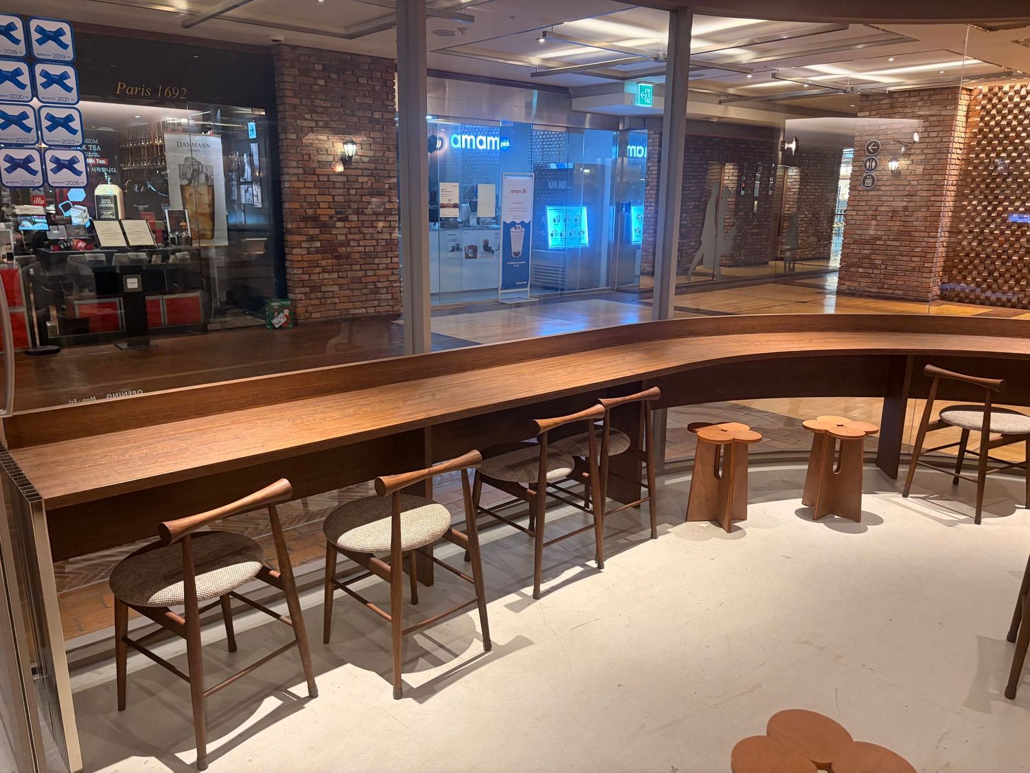 Modern curved wooden bar counter with cushioned chairs and rustic brick wall backdrop in a stylish restaurant interior.