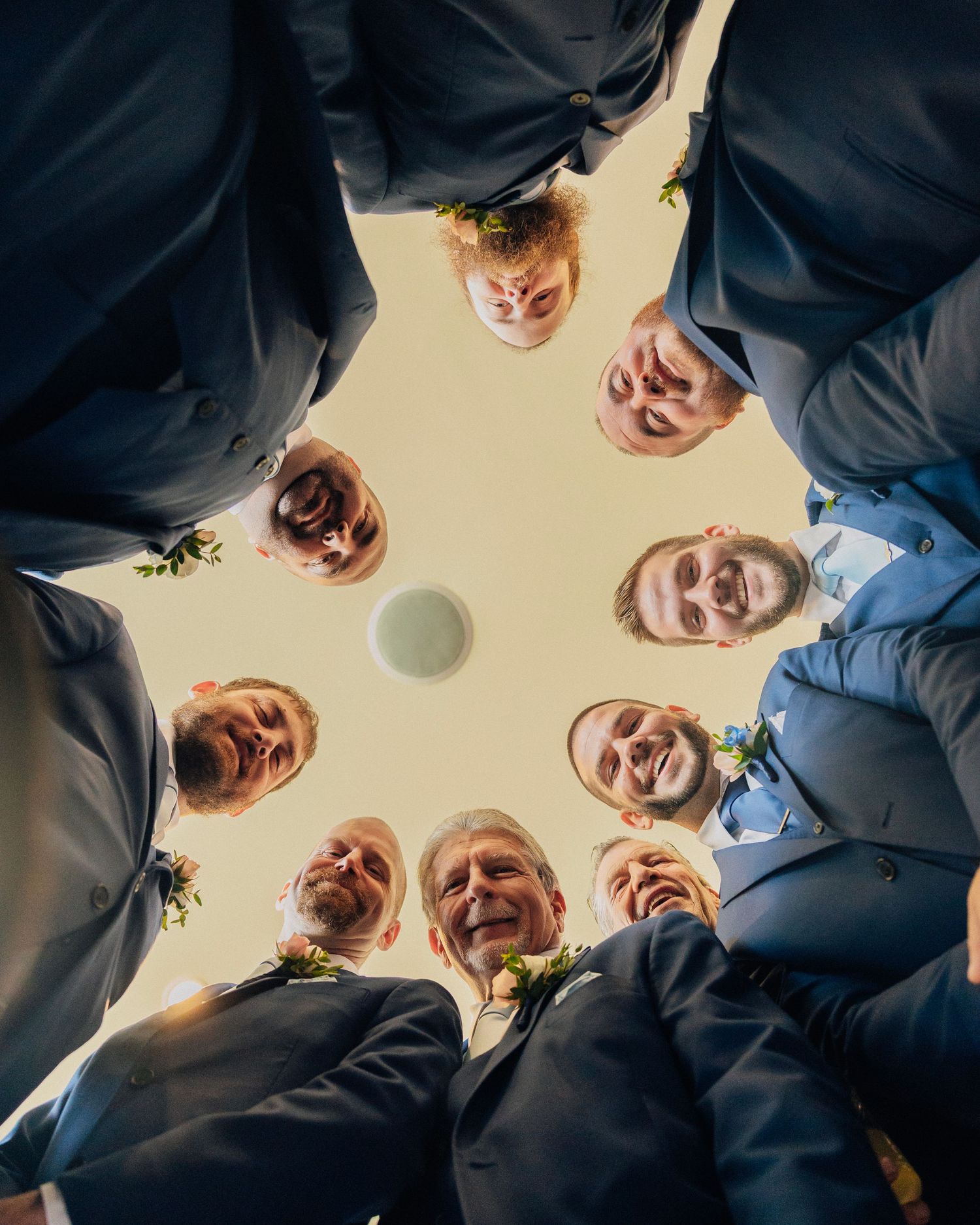 Creative low-angle shot of grinning groomsmen in navy suits forming a circle overhead.