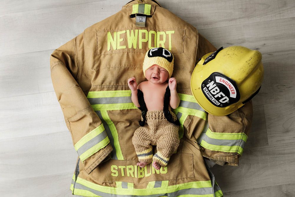 Newborn baby posed on firefighter turnout gear with yellow helmet for Newport STRIBLING.