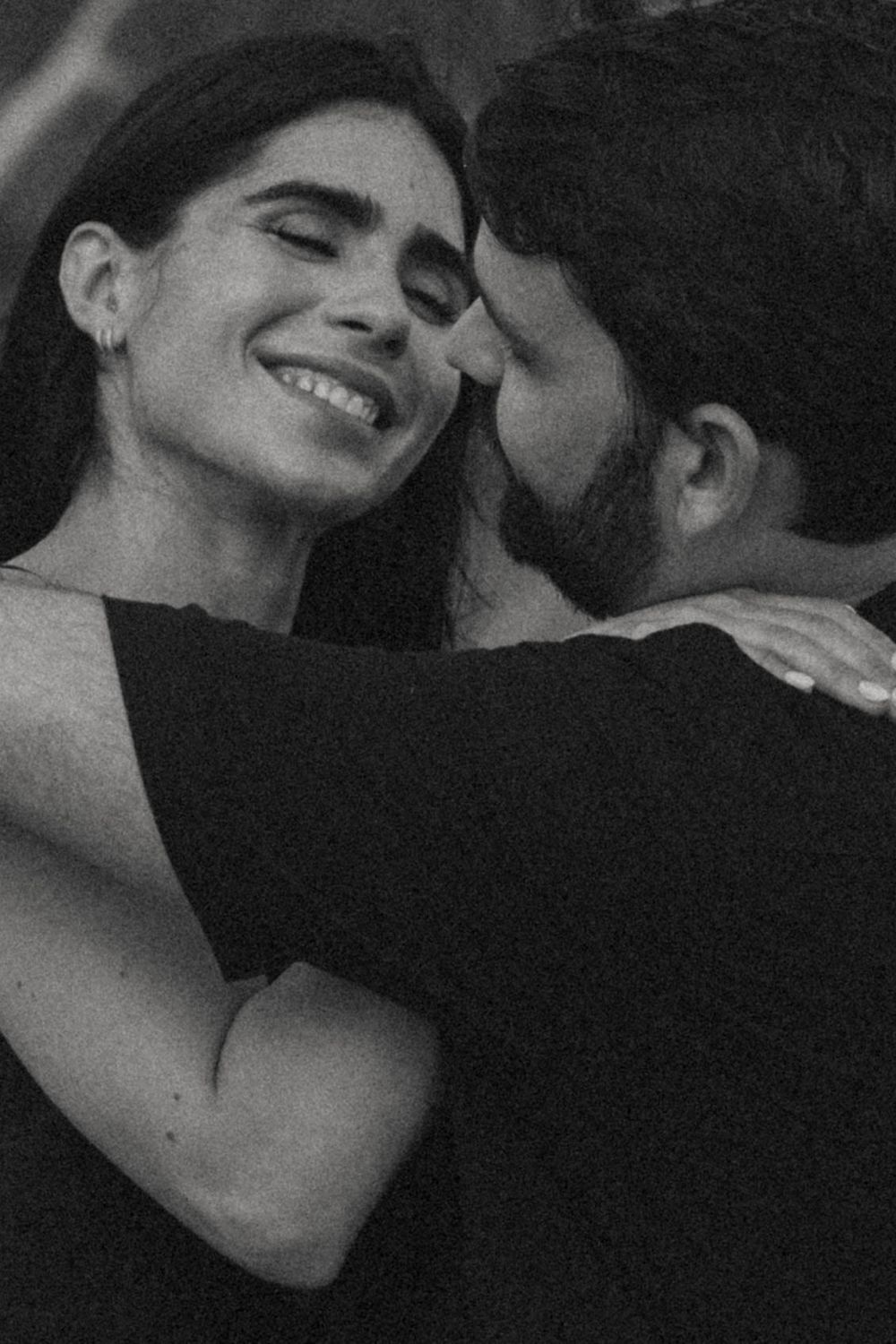 Black and white photo of a smiling woman embracing a man, sharing a tender romantic moment.