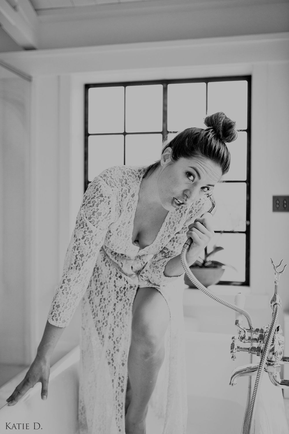 Black and white photo of a woman in a lace robe leaning over a bathtub near a window.