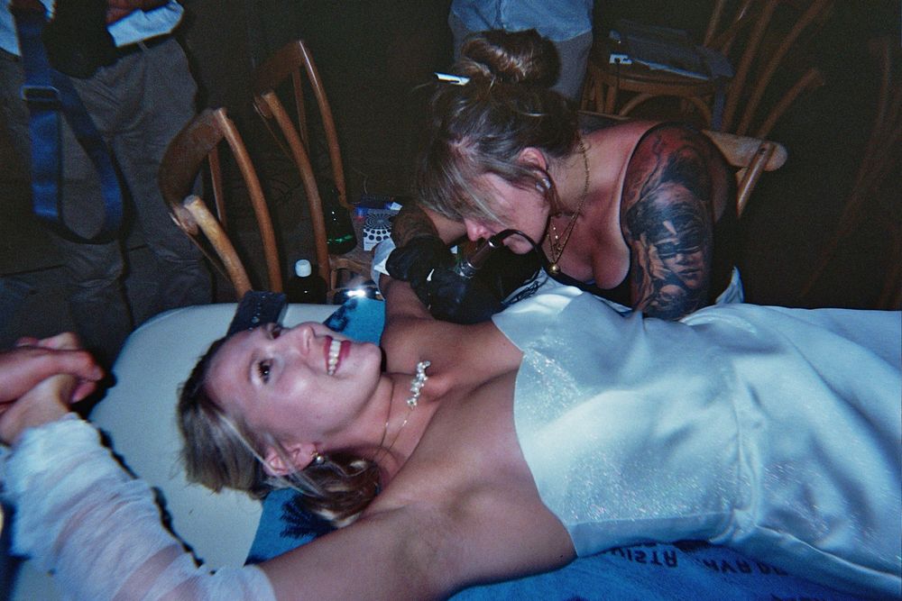 Two women laughing and posing together at a party, one lying down while the other leans over her smiling.