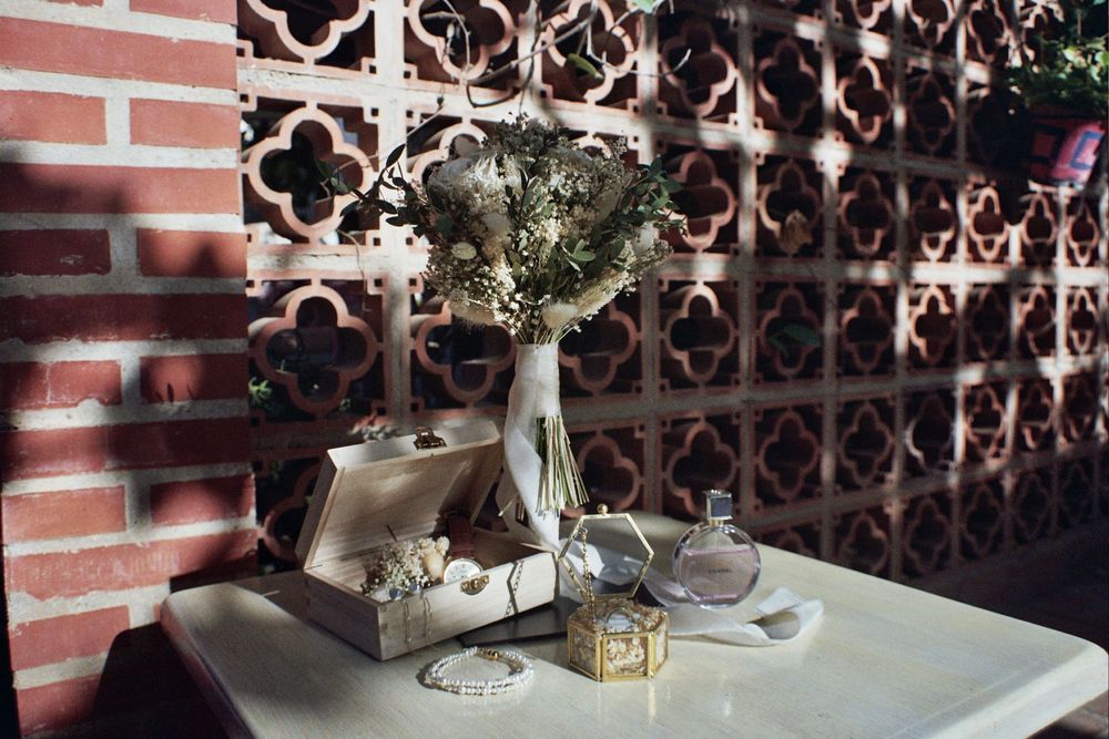Elegant table display with dried flowers in vase, perfume bottles, and decorative box against ornate brick wall.