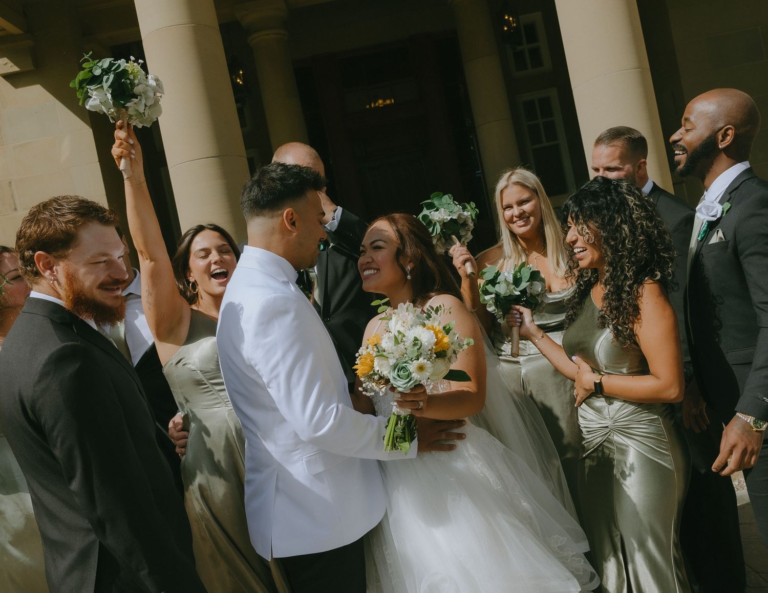 Bridesmaids in peach dresses hold bouquets up against a bright sky.
