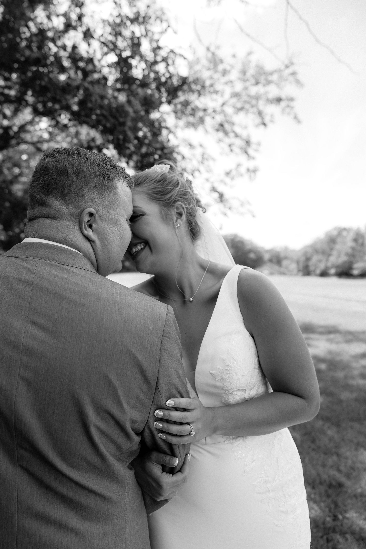 Romantic black and white wedding portrait under trees with lace dress and bouquet.
