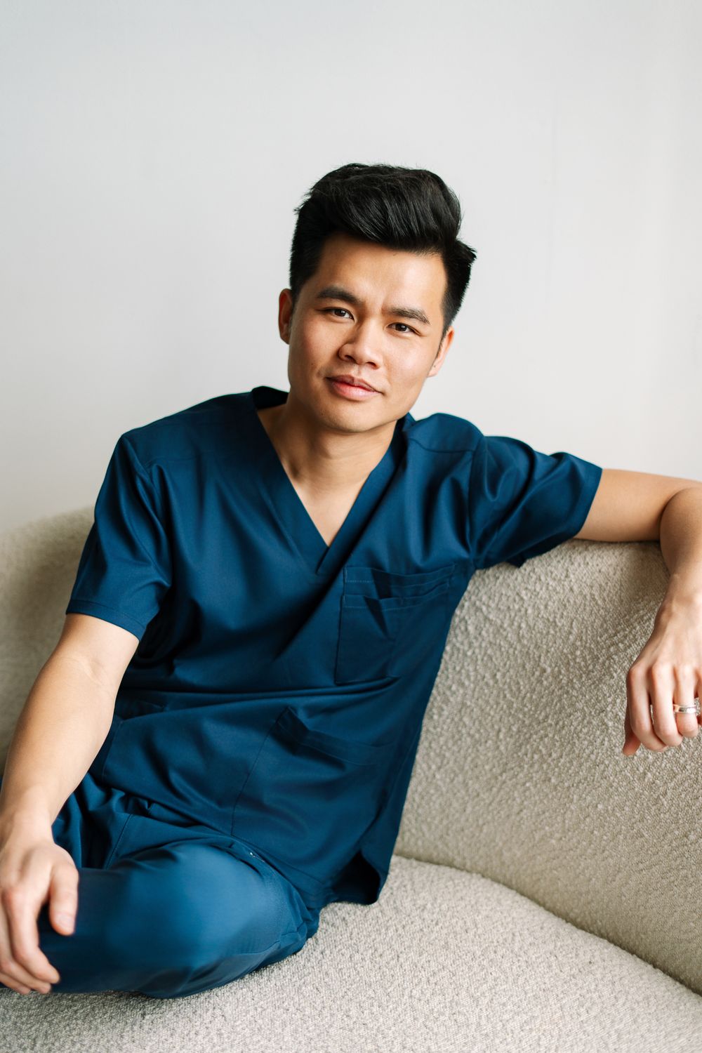 Male nurse in blue scrubs relaxing on a cream couch with a calm expression.
