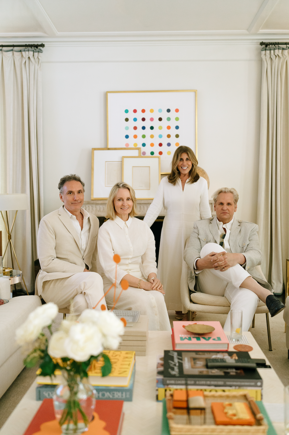 Four elegantly dressed people posing in a bright white living room with art.