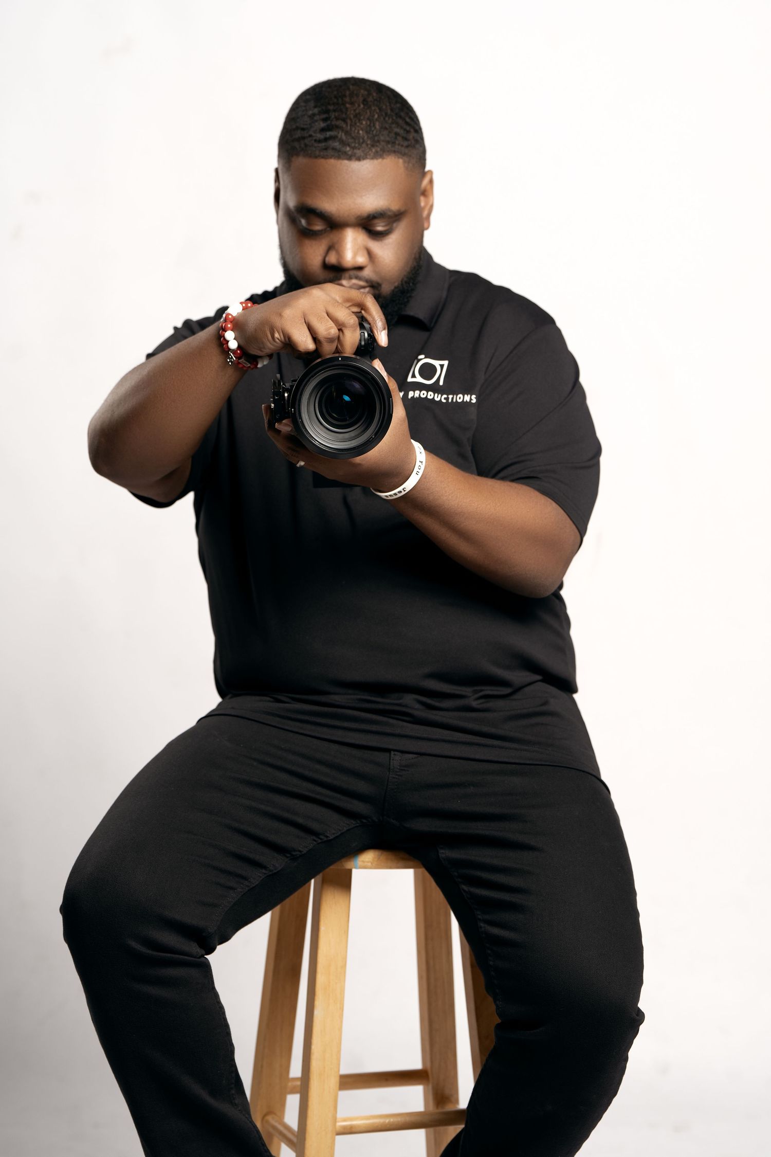 Photographer in casual black outfit posing with professional camera equipment.