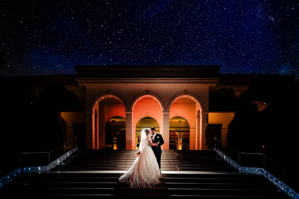 Newlywed couple embraces on grand illuminated steps under a starry night sky, creating a breathtaking and romantic wedding scene.