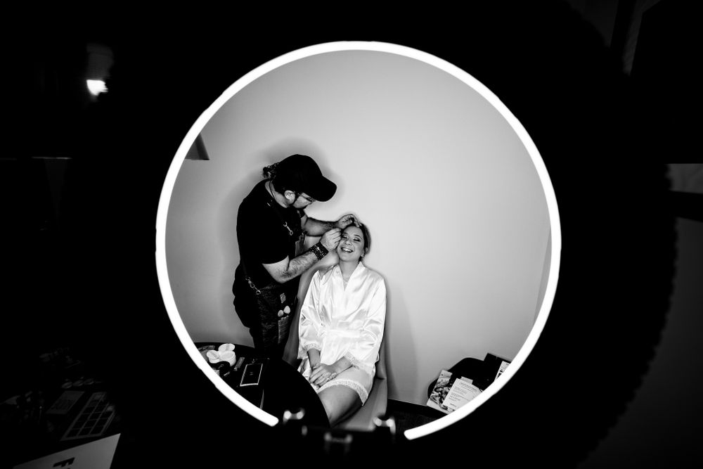 Black and white photo of bride getting her makeup done, framed artistically through a ring light, capturing a unique and intimate moment.