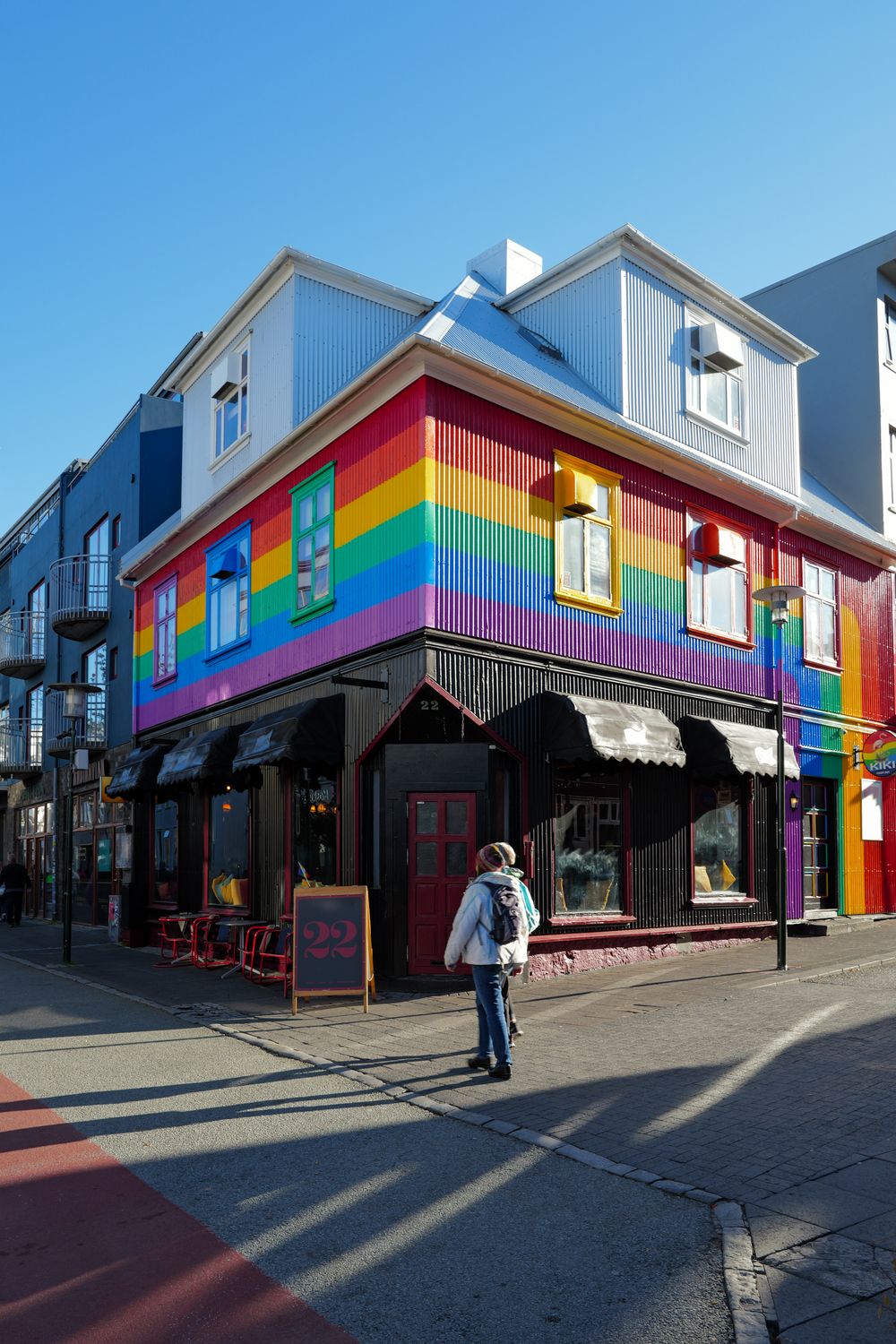 Vibrant rainbow-colored building exterior with striped paint design on a sunny urban street corner.