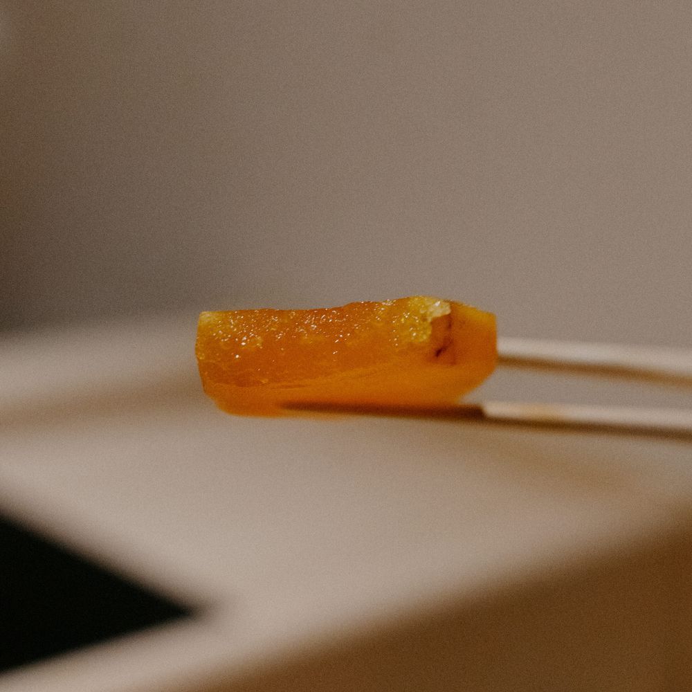 Close-up of an amber-colored piece of fish or garnish held with chopsticks.