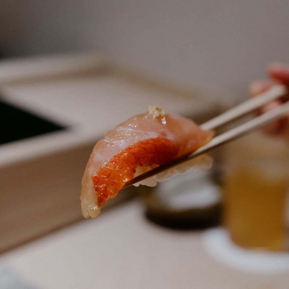 Fresh salmon nigiri sushi piece being held with chopsticks.