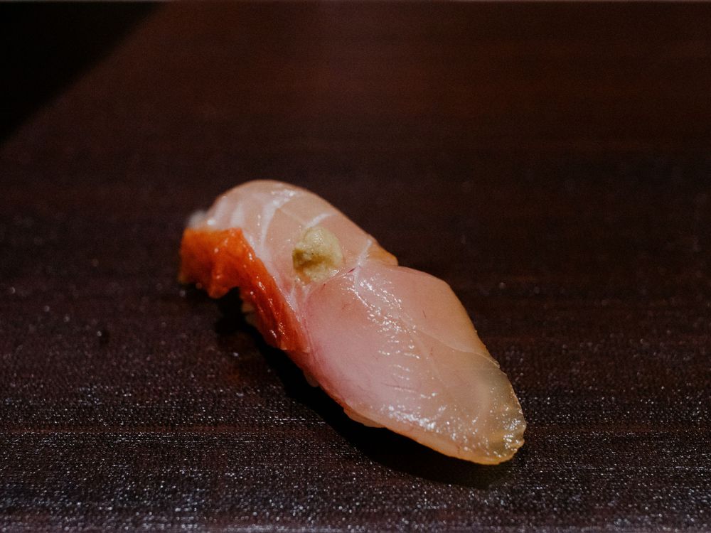 Close-up of a perfectly sliced piece of raw fish nigiri on a dark plate.