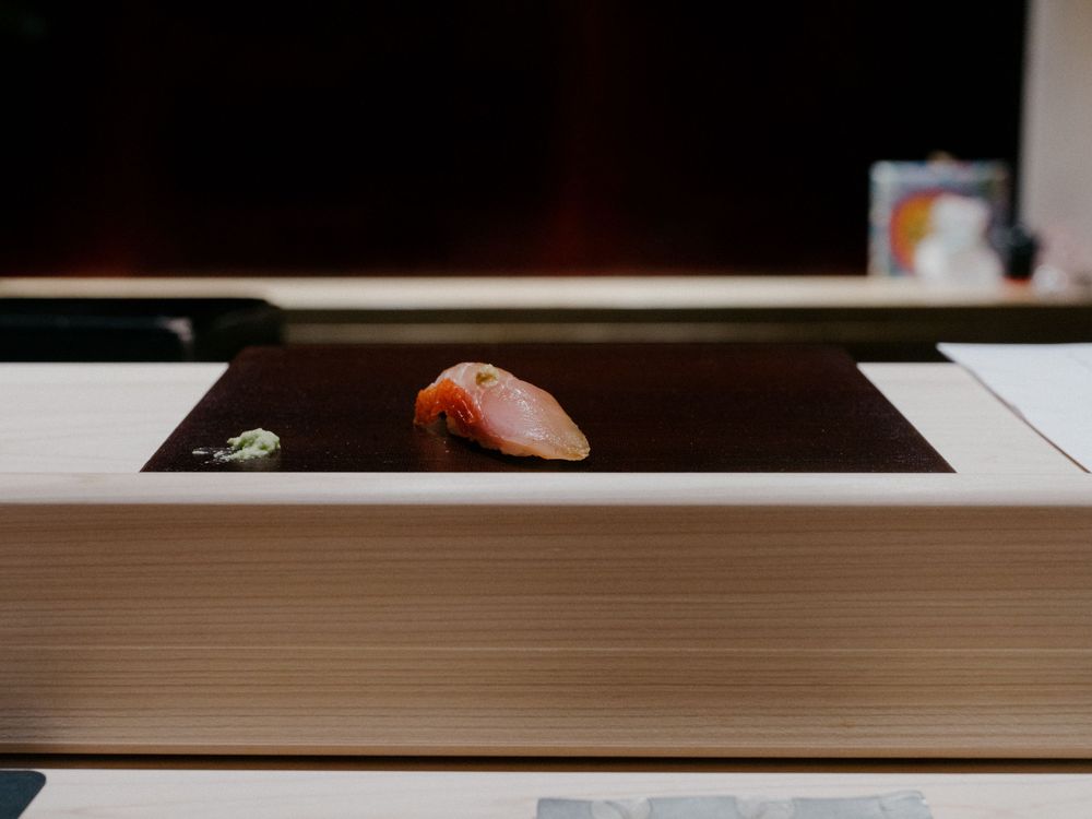 A single piece of salmon nigiri sushi presented on a dark surface.