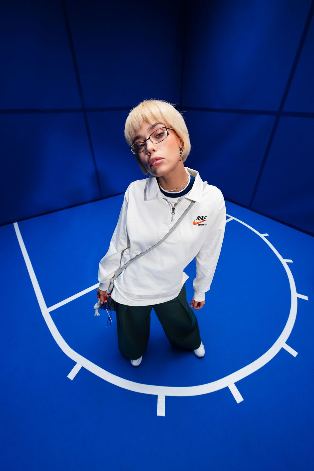 Sneaker campaign photo of a person in a white tracksuit standing on a blue indoor basketball court with circular floor marking