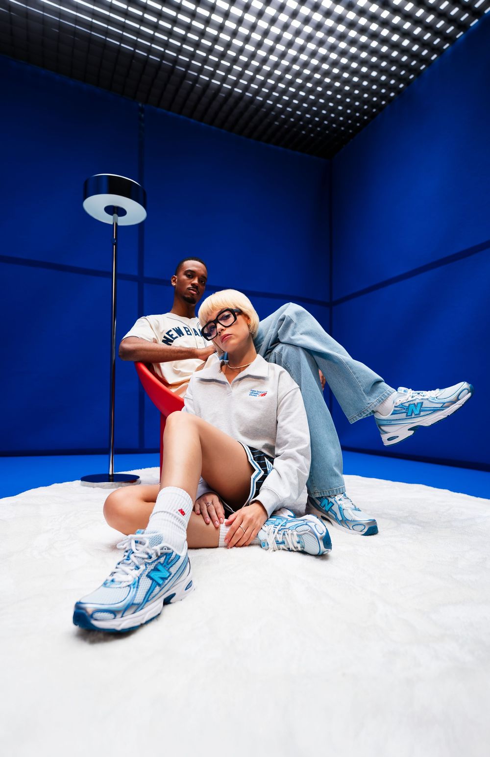 Fashion portrait of a person in grey outfit sitting on the floor in a bold blue geometric studio setting