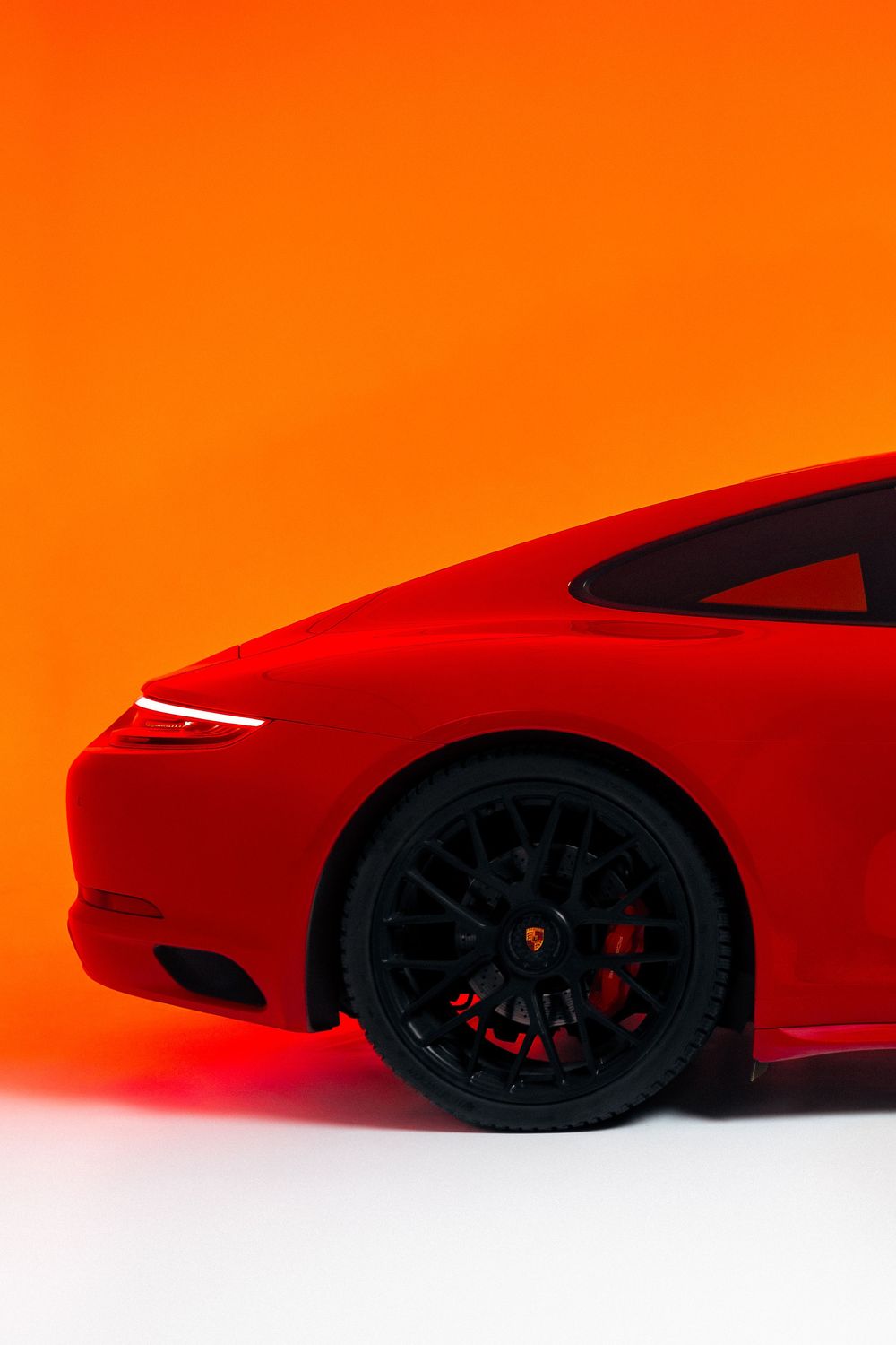 Minimalist product photo of a red Porsche sports car against a vibrant orange-red studio background