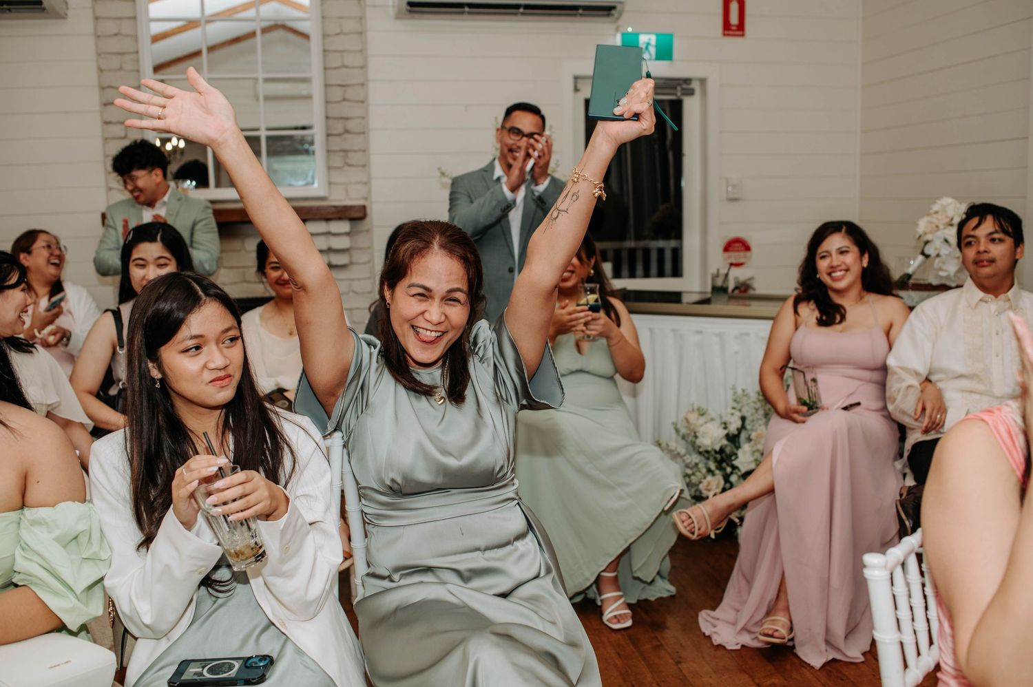Wedding guests in formal attire dancing enthusiastically during reception party.
