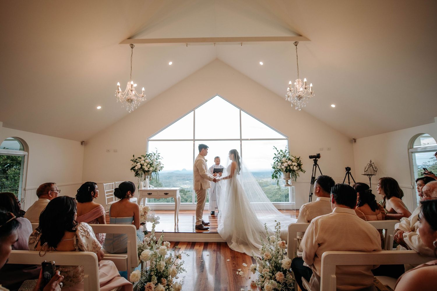 A wedding ceremony in a chapel with vaulted ceilings and large windows overlooking scenic views.