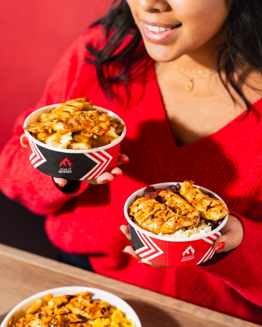 Three red and black branded bowls filled with crispy chicken and rice on a wooden surface against a red background.