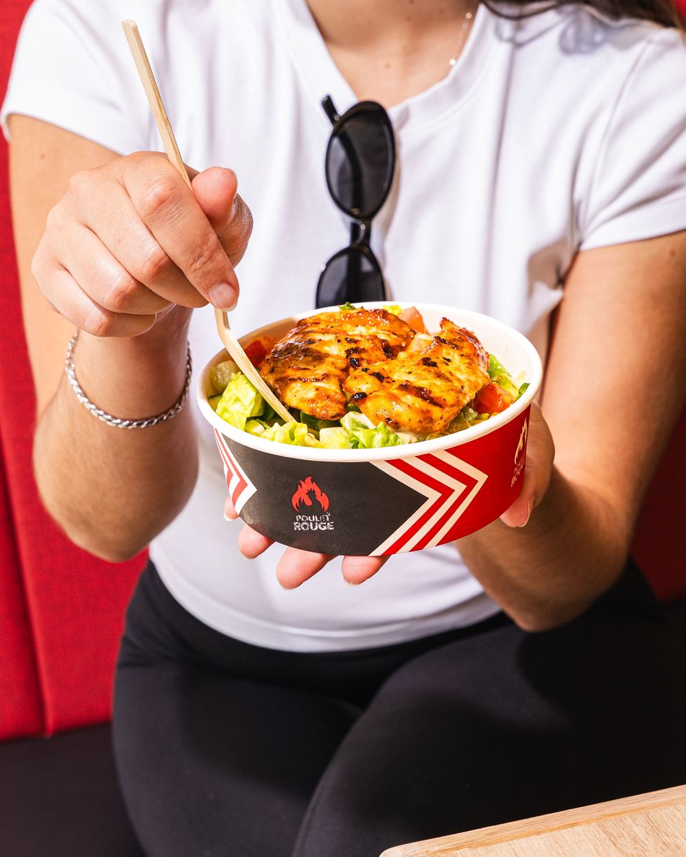 Woman holding a grilled chicken rice bowl with chopsticks from Poulet Rouge restaurant.