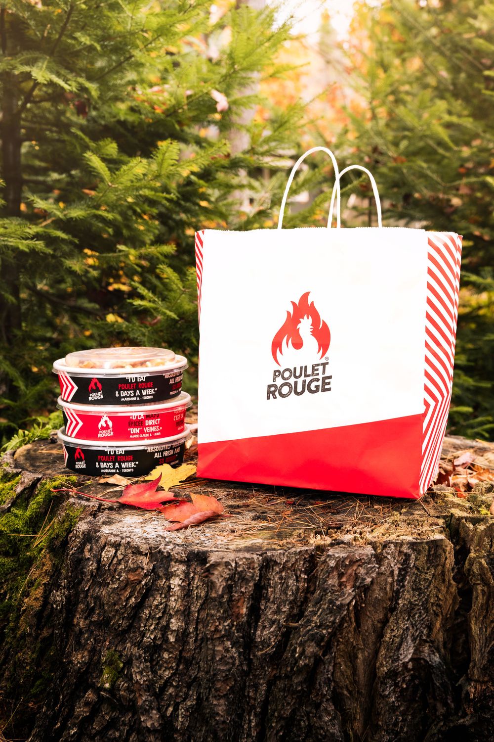 Poulet Rouge branded takeout bag and containers displayed on a rustic tree stump outdoors. Mtlshutter photography