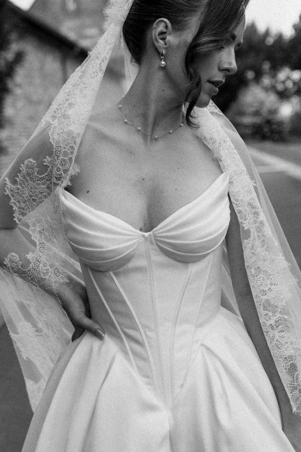 Black and white photo of a bride in a strapless corset wedding gown with lace veil and pearl necklace.