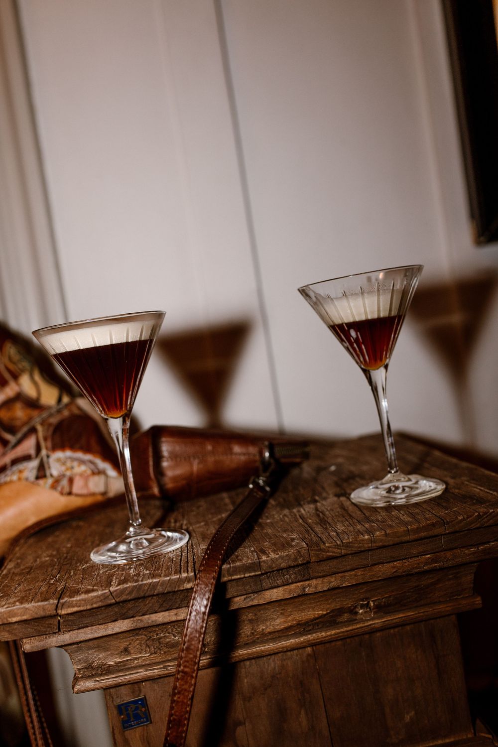 Two espresso martini cocktails in elegant stemmed glasses rest on a rustic wooden chest.