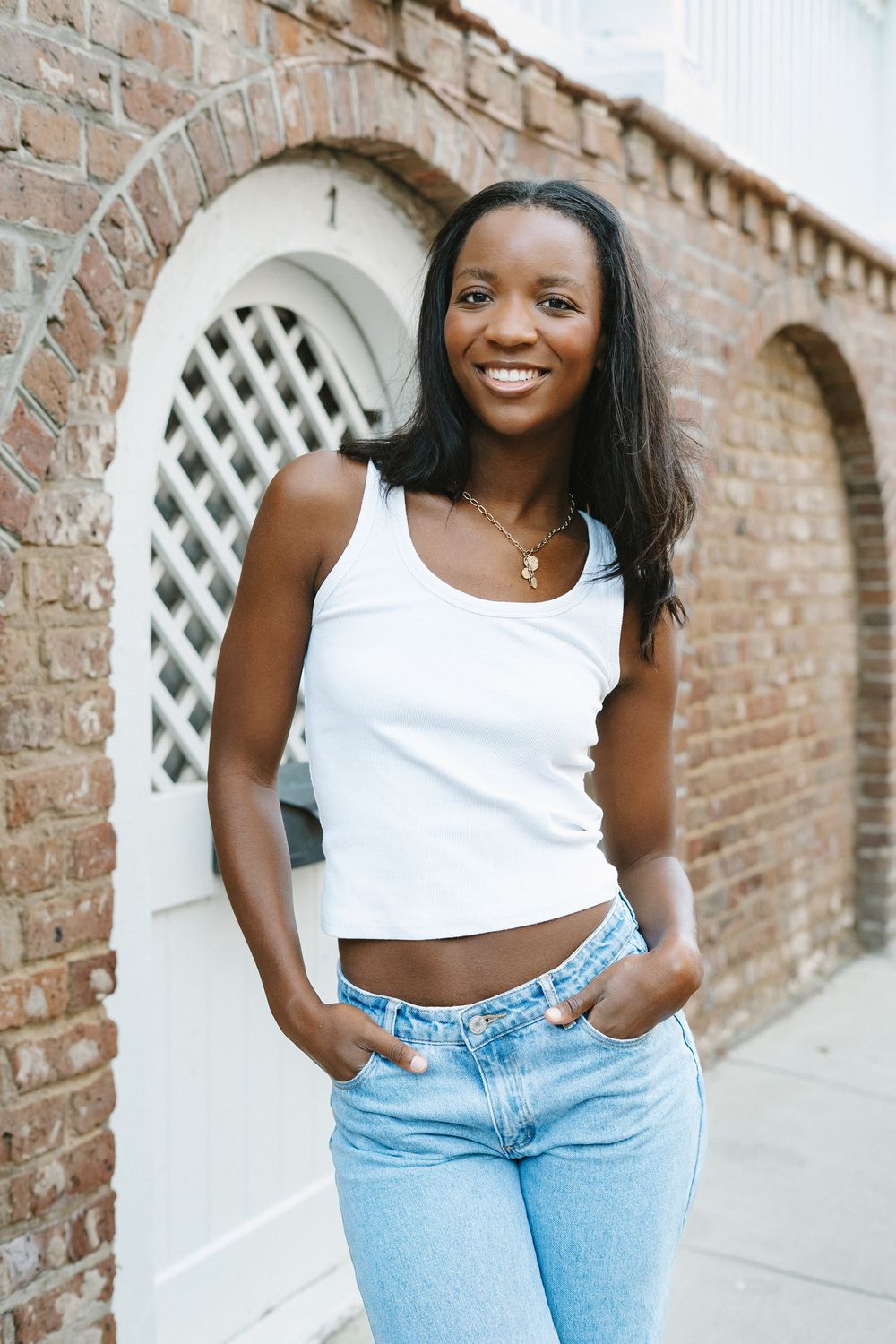 Casual summer fashion with white crop top and light blue jeans against a brick wall background.